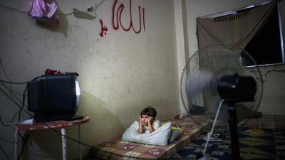 A young child is transfixed by the flashing television screen in his family's makeshift home.