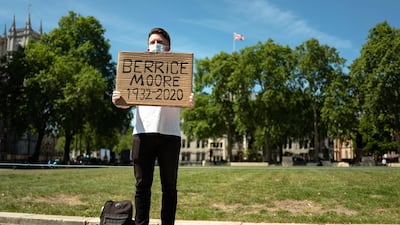 Ellis Tustin, the grandson of Berrice Moore, holds up his grandfather's name as he stages a personal protest against Prime Minister Boris Johnson outside the Houses of Parliament in May. Mr Tustin believes that the government is forgetting that each of the figures listed in the daily death toll update is a real person. He is displaying the name as Mr Johnson passes on the way to and from the weekly PMQ session. Getty Images