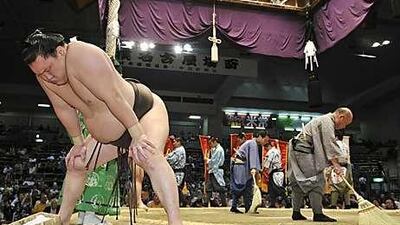 Hakuho, the Mongolian sumo grand champion, left, prepares as six banners of rewards for the bout's winner are shown on the ring.