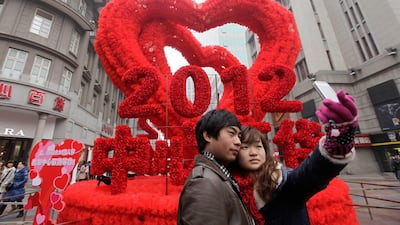 A couple takes a photograph with a mobile phone in front of a red heart decoration on the Valentine's Day in Wuhan, Hubei province February 14, 2012. REUTERS/Stringer