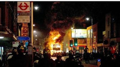 A double decker bus burns as riot police try to contain a large group of people on a main road in Tottenham, north London on August 6 2011. Two police cars were on Saturday set ablaze in north London following a protest over the fatal shooting of a 29-year-old man in an armed stand-off with officers. The patrol cars were torched as dozens gathered outside the police station on the High Road in Tottenham.