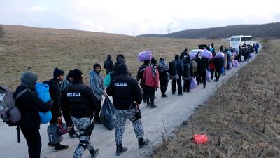 Police officers walk by migrants as they leave to be relocated from the Lipa camp. AP Photo