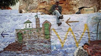 Men sit on a painted wall behind Bab el Bahr gates of Rabat’s Medina.