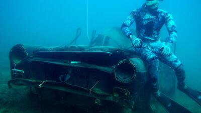 A diver poses next to a sunk car.