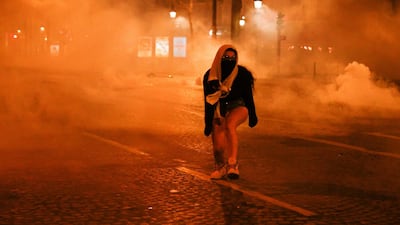 A woman walks covered as PSG supporters flee tear gas canisters on the Champs-Elysees. AFP