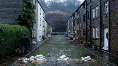 A man walks his dog past depleted sand bags which have been placed to protect Market Street in Walsden. EPA