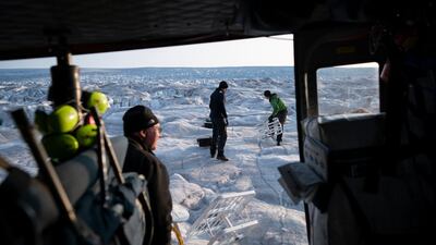 New York University air and ocean scientist David Holland, left, and field safety officer Brian Rougeux, right, are helped by pilot Martin Norregaard as they carry antennas out of a helicopter to be installed at the Helheim glacier.