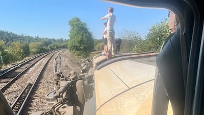 Passengers stand on the side of the derailed train, with apparently buckled tracks visible. Photo: Jeremy Veitch / X