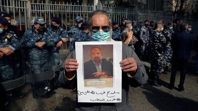 An anti-Hezbollah protester holds a picture of Lokman Slim, a longtime Shiite political activist and researcher, who has been found dead in his car, during a protest in front of the Justice Palace in BeirutBeirut, Lebanon, Thursday, Feb. 4, 2021. The Arabic words on poster read "Hezbollah's arms against who? Weapons of terrorism." (AP Photo/Bilal Hussein)