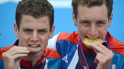 2012 Olympic gold medallist Alistair Brownlee, right, and his brother, bronze medallist Jonathan Brownlee, bite their medals as they celebrate on the podium of the men's triathlon event in London. The brothers will compete in the Abu Dhabi International Triathlon on Saturday. AFP PHOTO / CHRISTOPHE SIMON