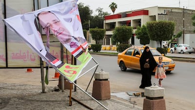 An Iraqi woman and a girl walk past an electoral banner for former Prime Minister Nouri Al Maliki that was damaged by a storm the day before, in the capital Baghdad on April 28, 2018. AFP
