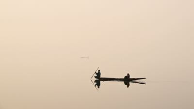 A man steers a boat across Dal Lake on a foggy day in Srinagar on December 12, 2023. (Photo by TAUSEEF MUSTAFA / AFP)
