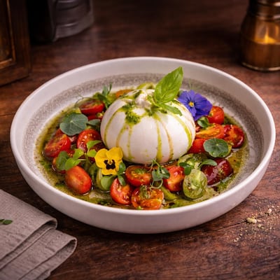 Creamy burrata decorated with heirloom tomatoes and pesto sauce. Photo: Readles by Chef Sperxos
