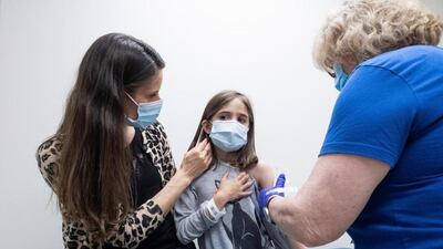 A child, 9, is held by her mother as she receives the second dose of the Pfizer vaccine during a clinical trial for children at Duke University in the US. Reuters