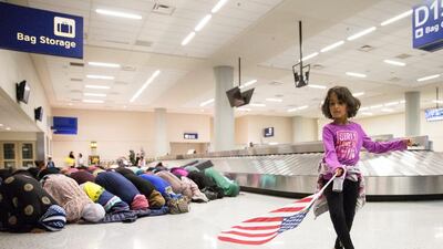 A girl dances with an American flag in baggage claim while women pray behind her during a protest against the travel ban imposed on seven Muslim countries by US president Donald Trump, at the Fort Worth International Airport in Dallas, Texas, on January 29, 2017. Laura Buckman / Reuters