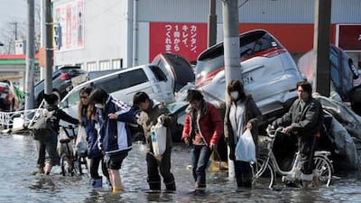 Against a backdrop of cars flipped by the tsunami, local residents wade through wate in the devastated main street in Ishinomaki, Miyagi prefecture, northern Japan.