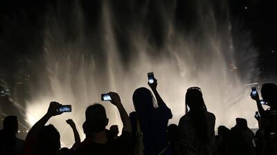Tourists take photos of the water and light show at the Burj Khalifa. Satish Kumar / The National