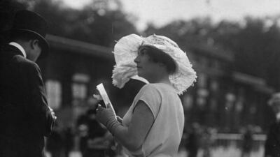 A women at Royal Ascot circa 1920 wears a white charmeuse and georgette Grecian dress, a wide-brimmed hat decorated with feathers and short gloves. Getty Images