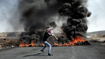 A Palestinian demonstrator uses a slingshot to throw stones towards Israeli security forces from behind burning tires during clashes in the West Bank town of Al-Bireh, on the northern outskirts of Ramallah. Thomas Coex / AFP