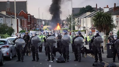 Riot officers hold back protesters near a burning police vehicle in Southport, England. Getty
