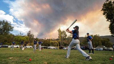 Little League players warm-up before a game as a brush fire is ablaze in back at a field next to the Sycuan Casino on the Sycuan Indian reservation during the Valley Fire, near Dehesa, in San Diego, California. AFP