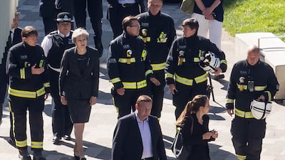 Members of the fire service join Ms May on a visit to Grenfell Tower in London, in June 2017, the day after at least 12 people were confirmed dead and dozens missing after the 24-storey tower was engulfed in flames