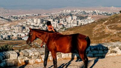 A man is seen with a horse in front of a view of Israel's controversial separation barrier between the West Bank village of al-Zaayem and Israel's largest Jewish settlement Maale Adumim. AFP