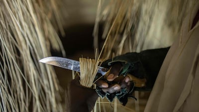 An artisan cuts thatching to be used in the reconstructed Kasubi Royal Tombs building.