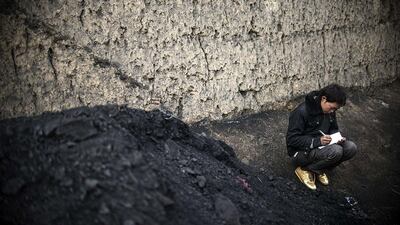An Afghan boy makes notes as he sits alongside a pile of coal from Samangan province.