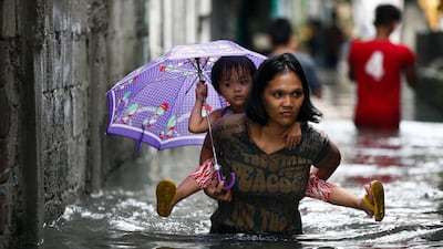 A woman carries a child on her back as they go through floodwaters in Quezon City, east of Manila. Rolex De La Pena / EPA