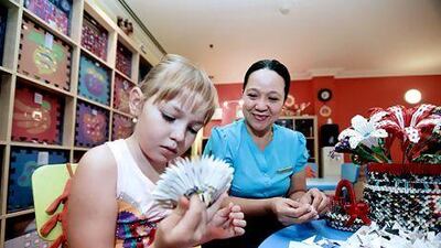 Raquel Perez, a kids' club attendant at The Ritz-Carlton Jumeirah, teaches paper crafts to Lisa Rudnikovskaya, 7. Sarah Dea / The National