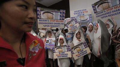 A Chinese restaurant attendant, left, stands next to a group of animal conservation activists wearing shark outfits during a protest outside a restaurant in Hong Kong. Kin Cheung / AP Photo