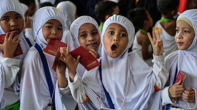 Hijab-clad Malaysian Muslim girls from the Little Caliphs kindergarten pose and gesture while holding their mock passports after completing an educational simulation of the Haj.