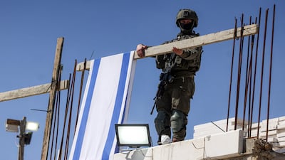 A soldier hangs an Israeli flag banner on a family home, taken over by settlers overnight, in Hebron, near the settlement area of Tel Rumeida, in the West Bank on March 24. AFP