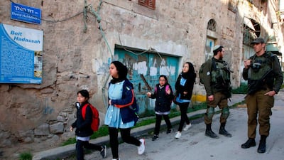 Palestinian schoolchildren walk past Israeli soldiers after forces closed a street near the settlement of Beit Hadassa in the divided West Bank city of Hebron. AFP