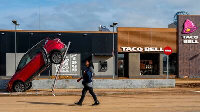 A woman walks past a car swept up a pole by flood water in Valencia, Spain. AP