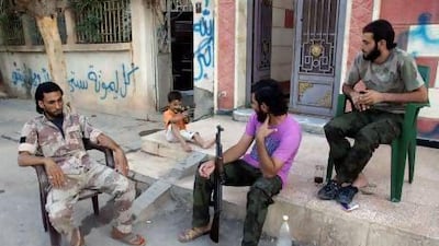 A boy aims his toy gun as he sits with members of the Free Syrian Army in Deir Al Zor.