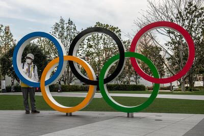 A woman wearing a face mask poses for a photograph next to the Olympic rings in Tokyo, Japan. Getty