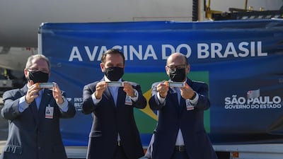 Sao Paulo Governor Joao Doria (C), Sao Paulo state Health Secretary Jean Gorinchteyn (L) and Butantan Institute director Dimas Covas (R), pose for photos holding doses of the CoronaVac vaccine against Covid-19 next to a container unloaded from a cargo plane that arrived from China to Sao Paulo airport. AFP