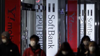 Pedestrians wearing facemasks walk past signs outside a Softbank store in Tokyo. The company is laying off 10% of overseas staff. Bloomberg