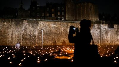 A woman photographs lit torches that are part of the installation 'Beyond the Deepening Shadow' at the Tower of London. Reuters