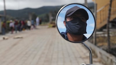A man wearing a mask to help curb the spread of the new coronavirus is reflected in the mirror of his motorcycle in Cariacu, Ecuador. AP Photo