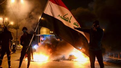 Masked anti-government protester wave the national flag before flaming tyres at a make-shift roadblock in the central Iraqi holy shrine city of Najaf. AFP