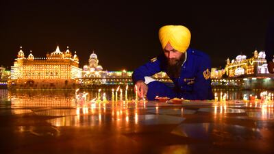 A Sikh man lights candles at an illuminated Golden temple on the eve of the birth anniversary of Guru Nanak in Amritsar, India. AP Photo
