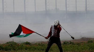 A masked demonstrator holding a Palestinian flag uses a sling to hurl stones at Israeli forces. Reuters