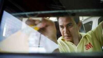 Raul Dela Cruz, a worker at the Goldem 3M shop in Abu Dhabi, applies tint to a car's window.