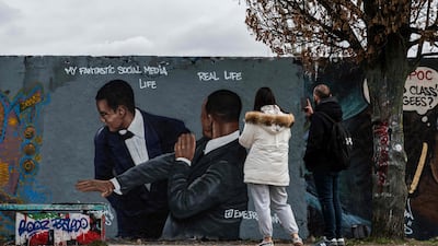 A couple take photos of a mural by Berlin street artist Eme Freethinker, depicting Will Smith slapping Chris Rock during the Oscars ceremony. AFP