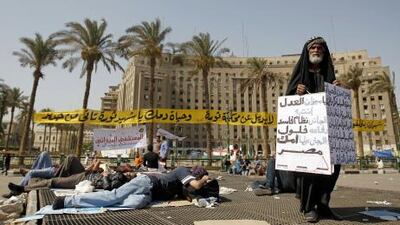 An elderly Egyptian protester holds a sign calling for justice for the sake of Egypt as other demonstrators sleep in Cairo's landmark Tahrir Square.