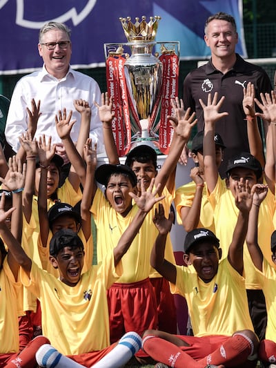 UK Prime Minister Keir Starmer and former England striker Michael Owen show the Premier League trophy to young players in Mumbai. AFP