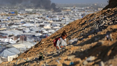 A girl climbs a hilltop against the backdrop of smoke rising from a shelter that housed displaced Palestinians after an Israeli air strike to the west of Khan Younis